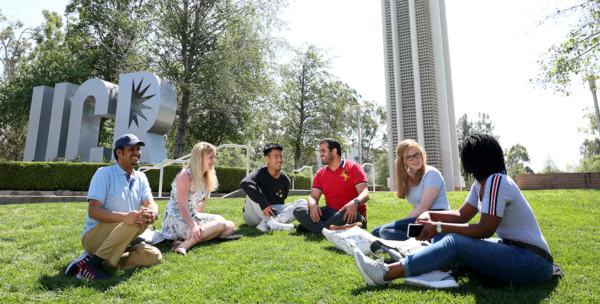 Group picture of students sitting in front of UCR Sign and Bell Tower